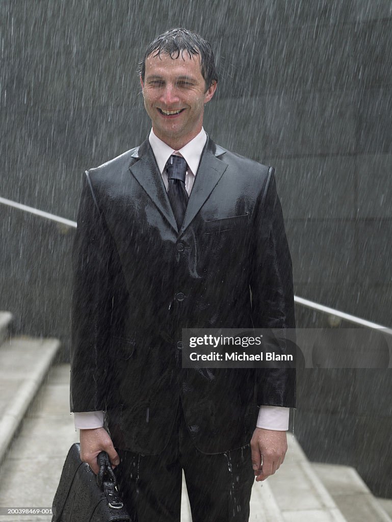 Businessman with briefcase standing on steps in rain, smiling, portrait