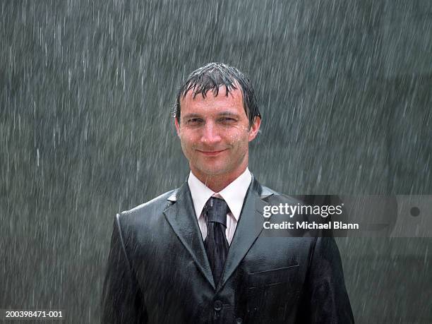 businessman standing in rain, smiling, portrait, close-up - doorweekt stockfoto's en -beelden