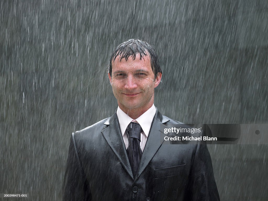 Businessman standing in rain, smiling, portrait, close-up