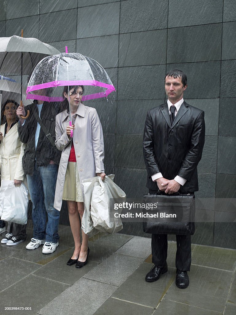 Young woman under umbrella looking over at soaked businessman