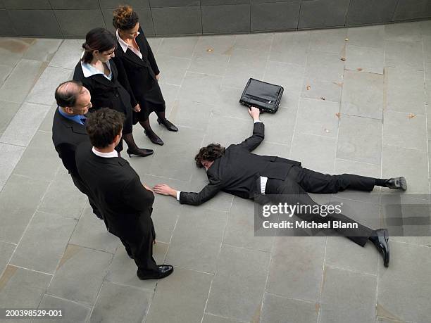 business people looking down at man lying on pavement, elevated view - bewusteloos stockfoto's en -beelden