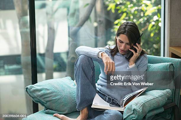 woman using mobile phone, and looking down at magazine - glass magazine stock-fotos und bilder