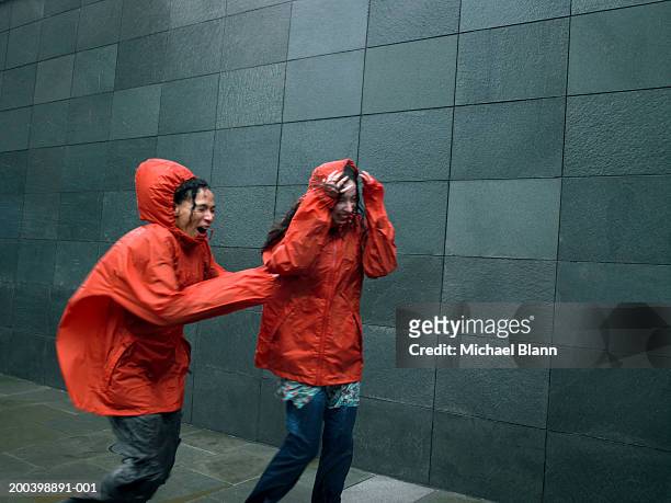 two women in anoraks struggling to walk against rainstorm, eyes closed - regenmantel stock-fotos und bilder