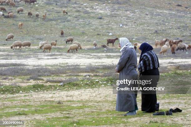 Jordanian couple perform noon prayers 07 February 2002 on the outskirts of Amman before boarding their buses to head for Mecca in Saudi Arabia. The...