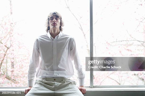 young man sitting on window sill, eyes closed - open collar stock pictures, royalty-free photos & images