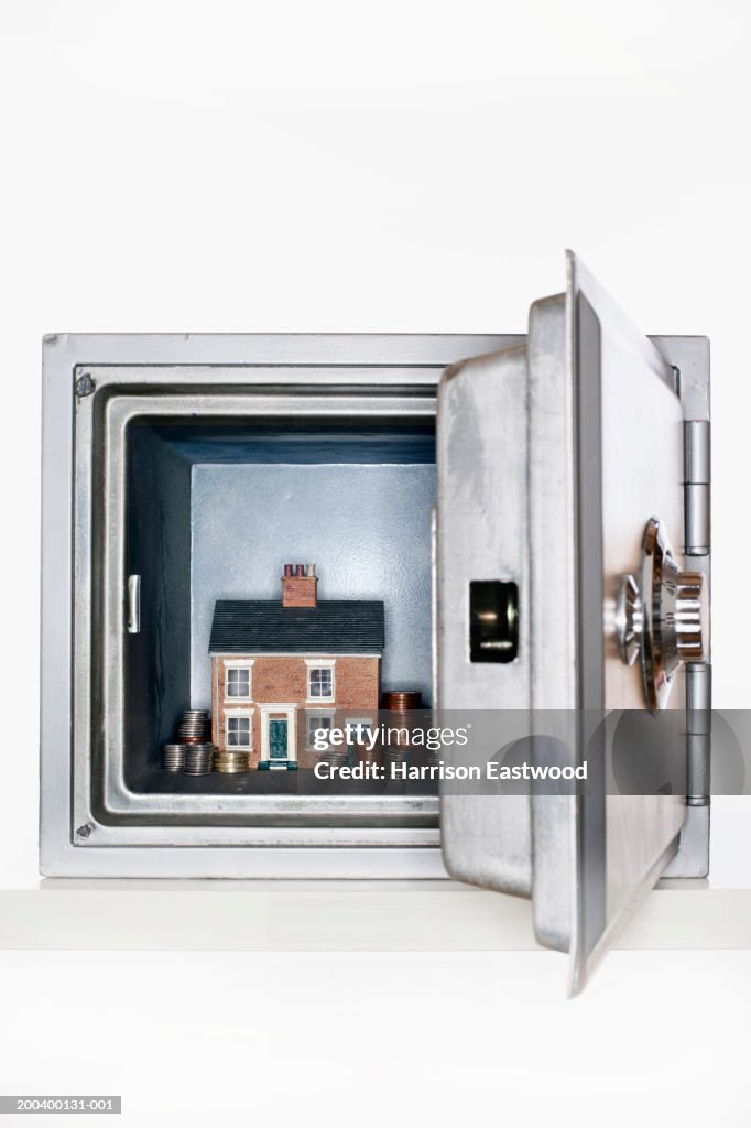 Model house and stacked coins in safe, view through open door