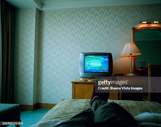 man lying on hotel room bed, watching television, low section - solo un uomo foto e immagini stock