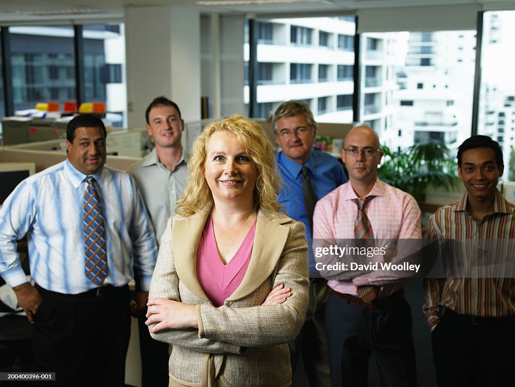 Businesswoman standing in front of male colleagues, smiling, portrait