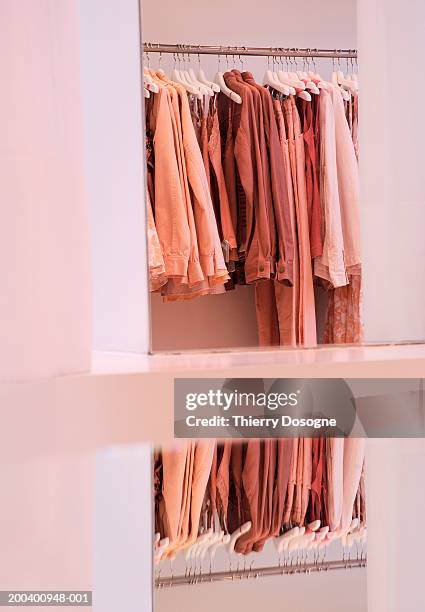 coats on hangers on rack in clothes shop reflected in mirror - clothes rack stock-fotos und bilder