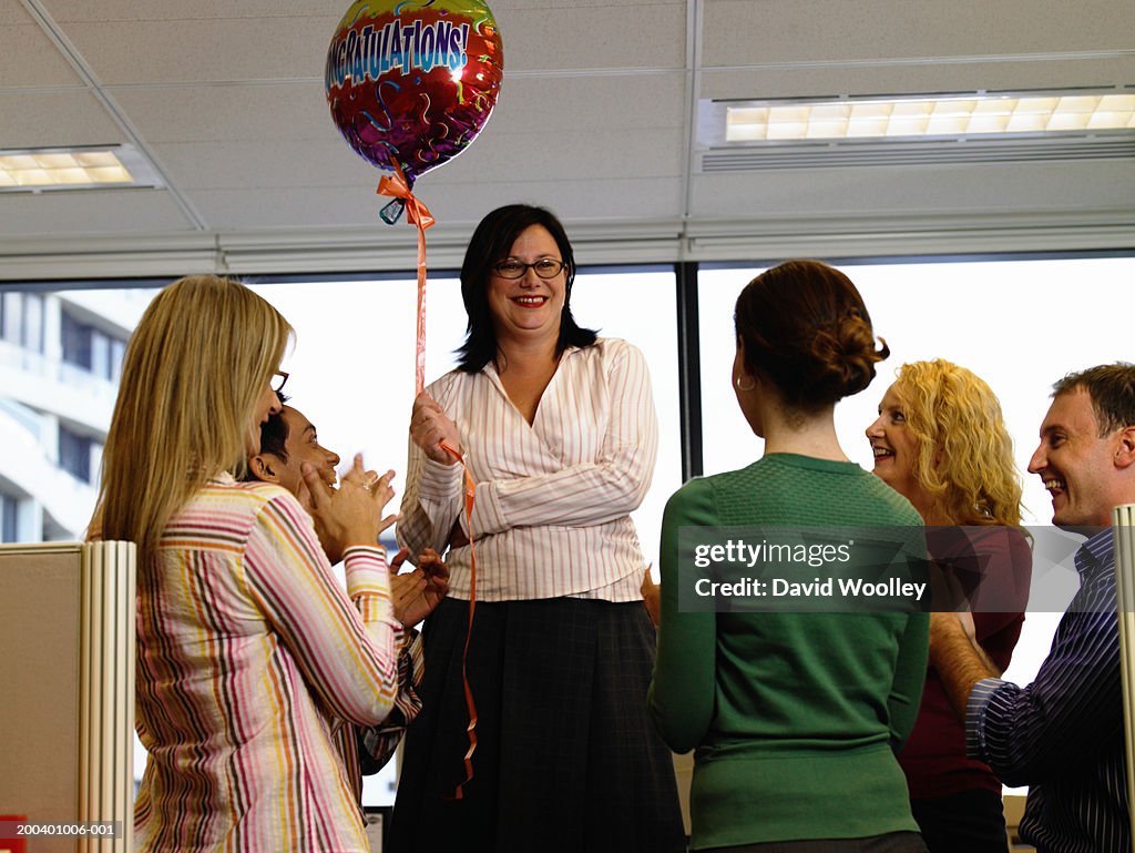 Colleagues applauding businesswoman holding 'congradulations' balloon