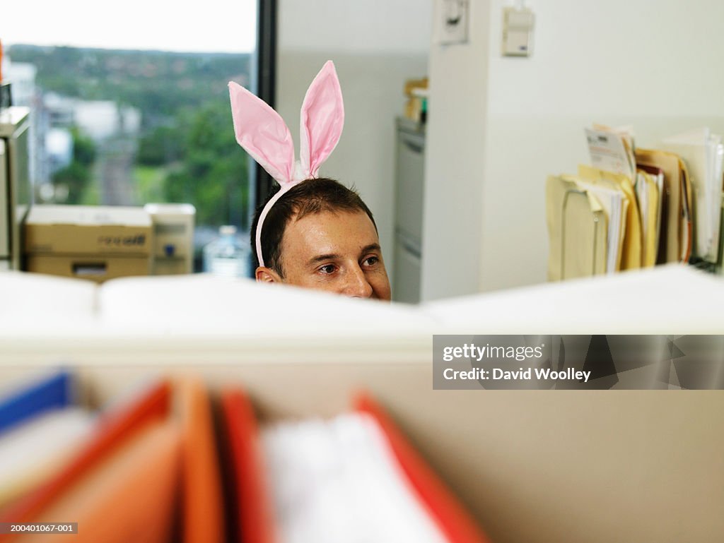 Man wearing bunny ears in office, desk divder in foreground