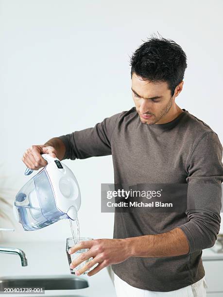 man in kitchen pouring glass of water from jug - jug stockfoto's en -beelden