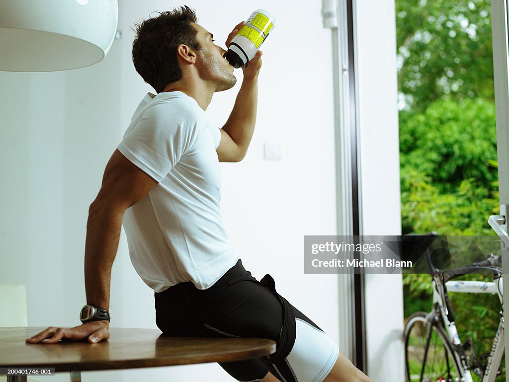 Man in sports clothes sitting on table, drinking from water bottle