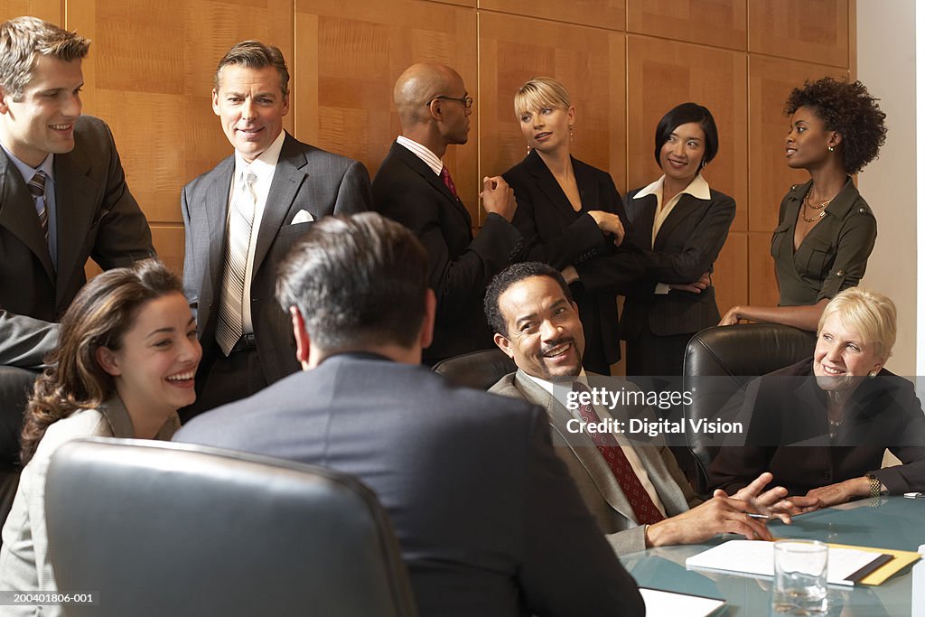 Businessmen and women conversing in conference room, smiling