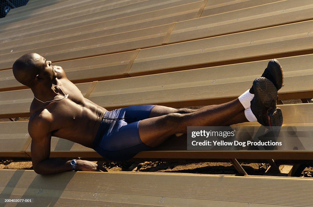Male athlete resting on stadium steps, side view