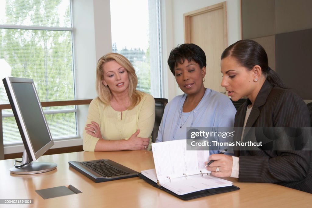 Three businesswomen looking at personal organizer during meeting