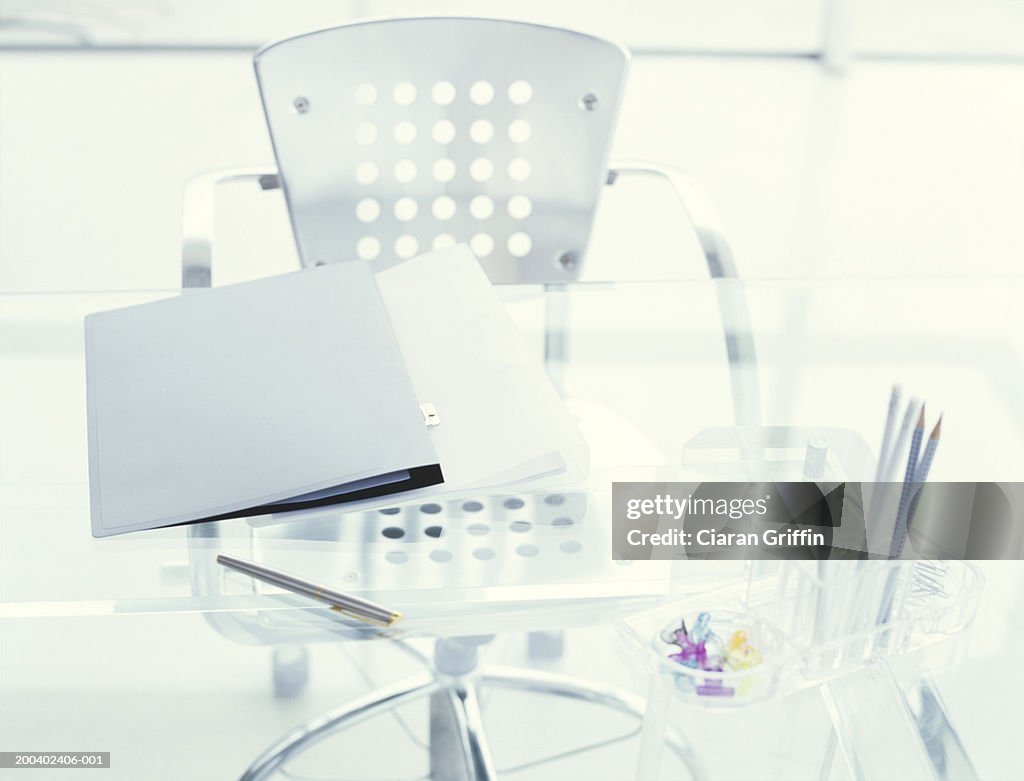 Pen holder and folder on glass table by chair, elevated view