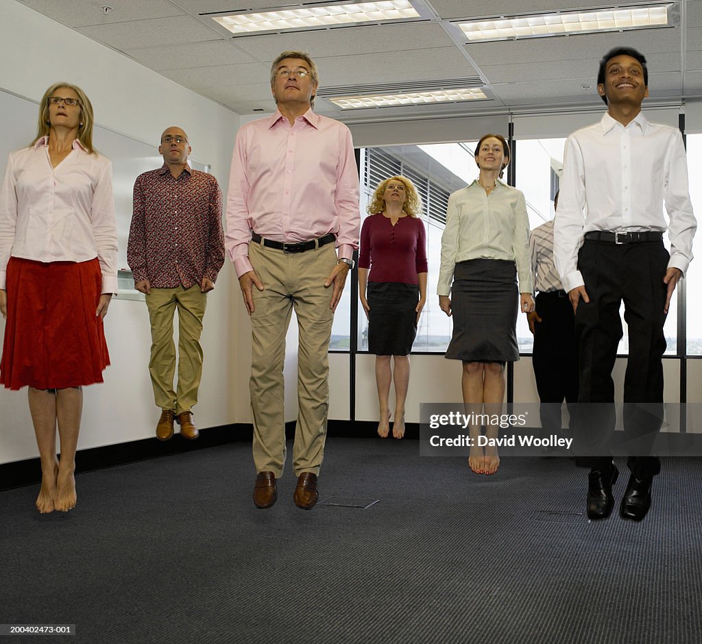 Office workers jumping in empty office, arms by side