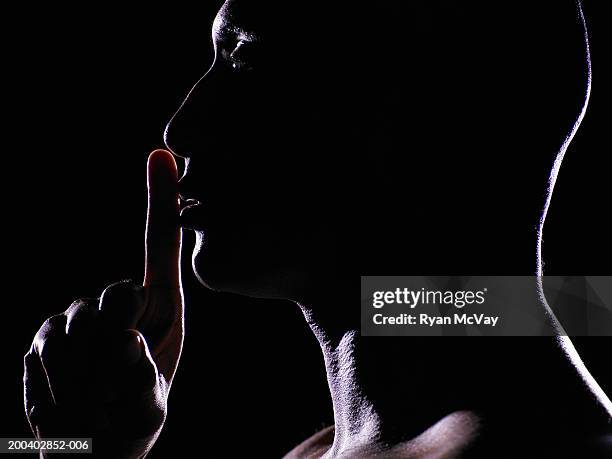 man with finger on lips, side view - silence foto e immagini stock