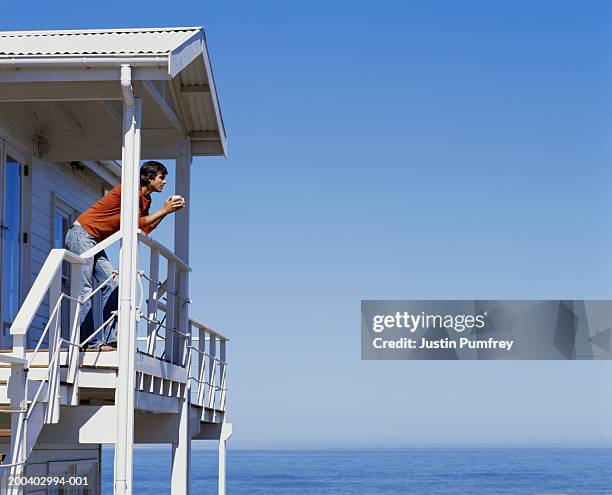 man leaning on balcony railing, holding cup, low angle view - casa al mare foto e immagini stock