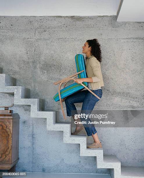 young woman carrying chair upstairs, side view - moving furniture stock pictures, royalty-free photos & images