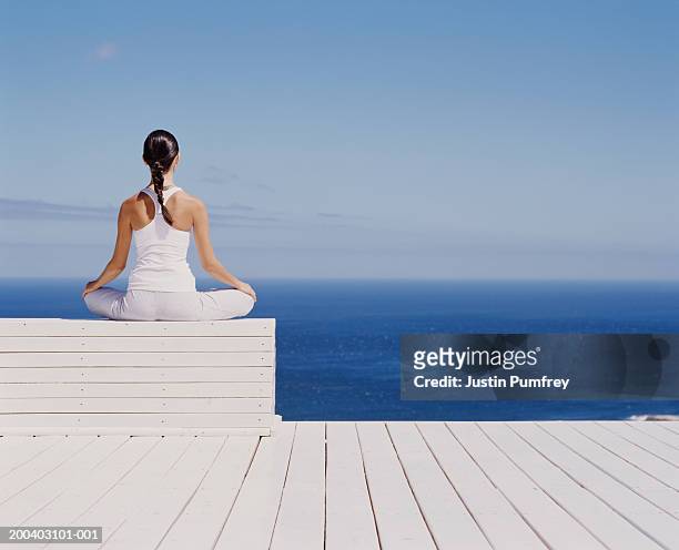 young woman meditating on wooden block, rear view - benessere foto e immagini stock