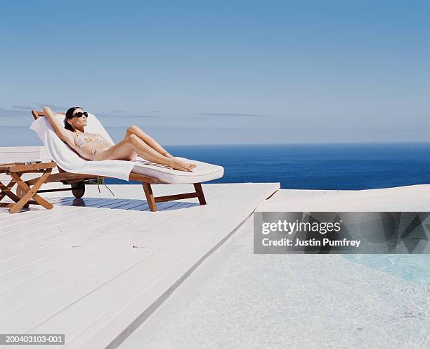 young woman at spa relaxing on sunlounger by outdoor pool - reclining chair stock pictures, royalty-free photos & images