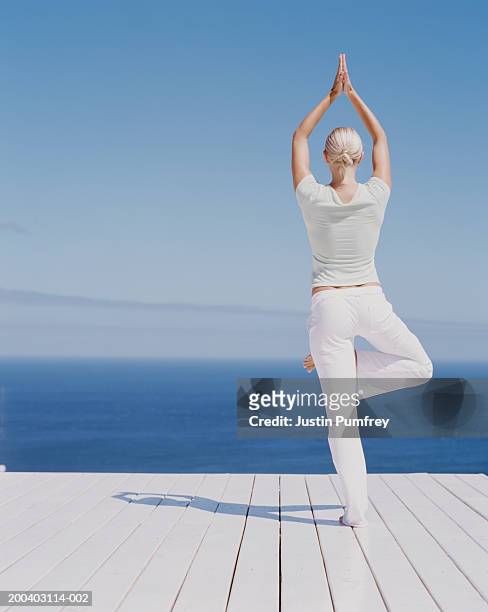 young woman performing tree pose on decking, rear view - white pants stock-fotos und bilder