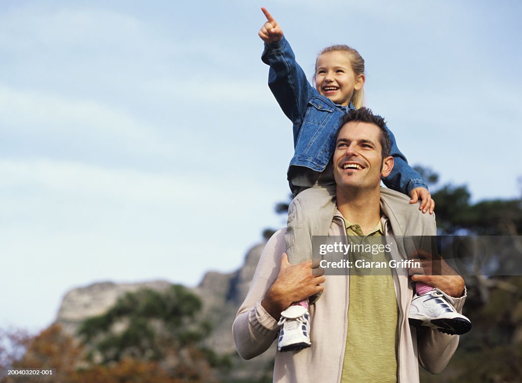 Girl (4-6) on man's shoulders, pointing, low angle