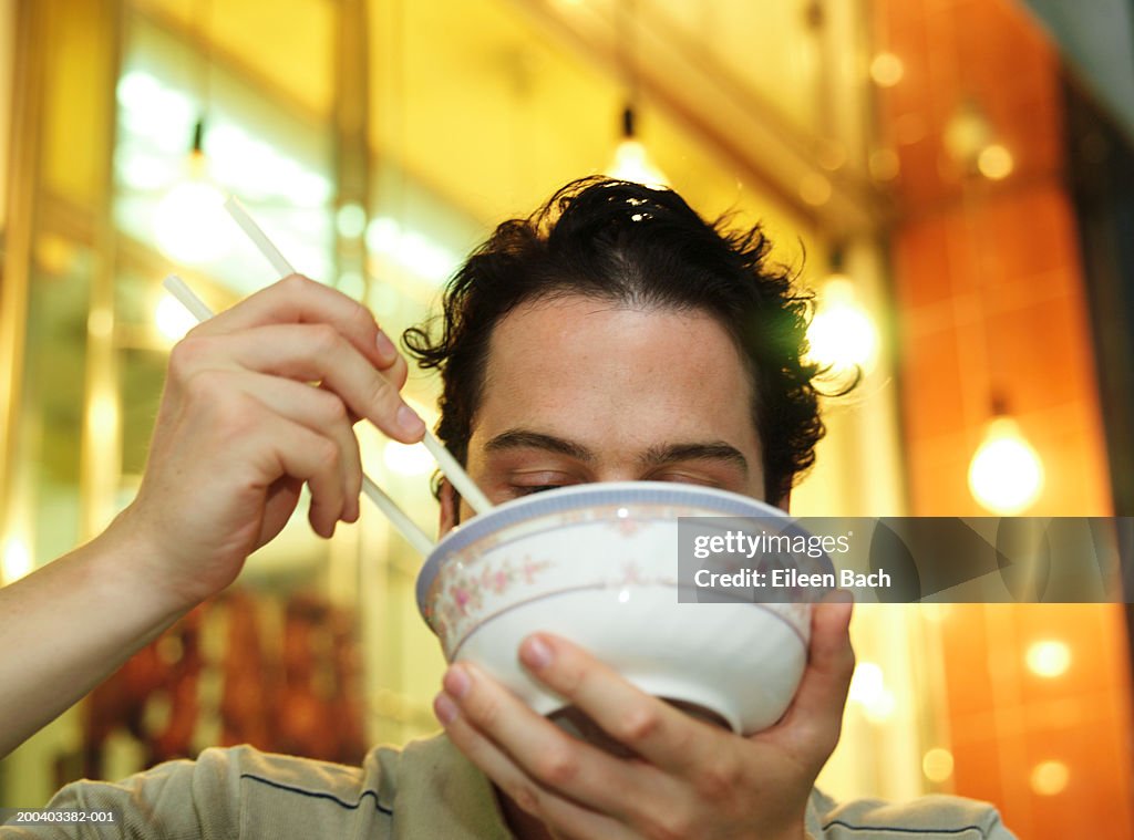 Man eating noodles, bowl obscuring face, low angle view