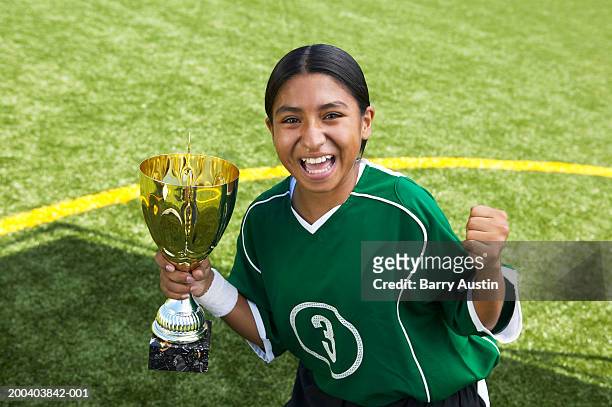 female (10-12) footballer with trophy, other hand making fist, smiling - girl 10 12 stock pictures, royalty-free photos & images