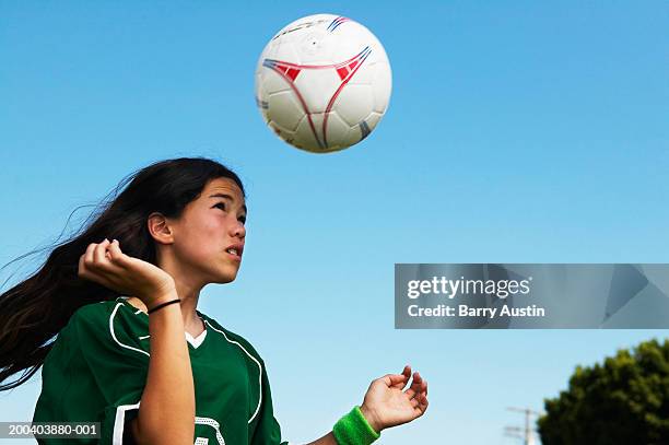 female footballer (11-13) heading ball, low angle view - heading the ball stockfoto's en -beelden