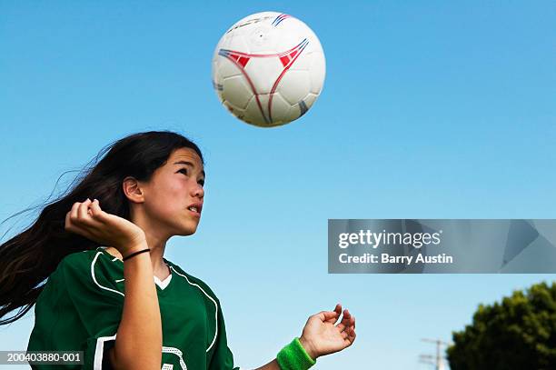 Female footballer (11-13) heading ball, low angle view