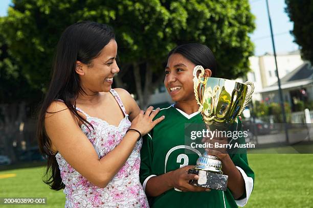 mother smiling at daughter (11-13) holding football trophy - teen awards stock pictures, royalty-free photos & images