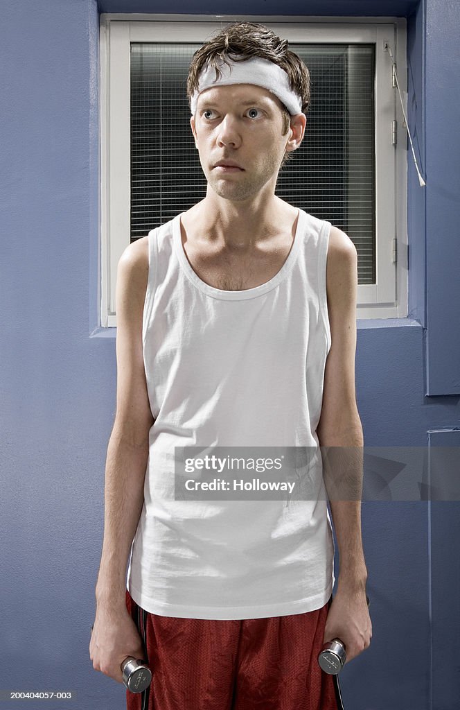 Man wearing sweatband in gym holding dumbbells by sides