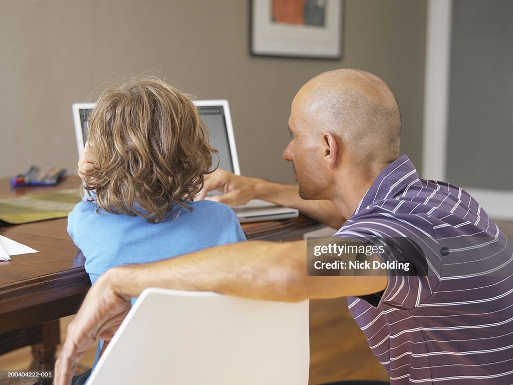 Father and son (4-6) using laptop on table, rear view