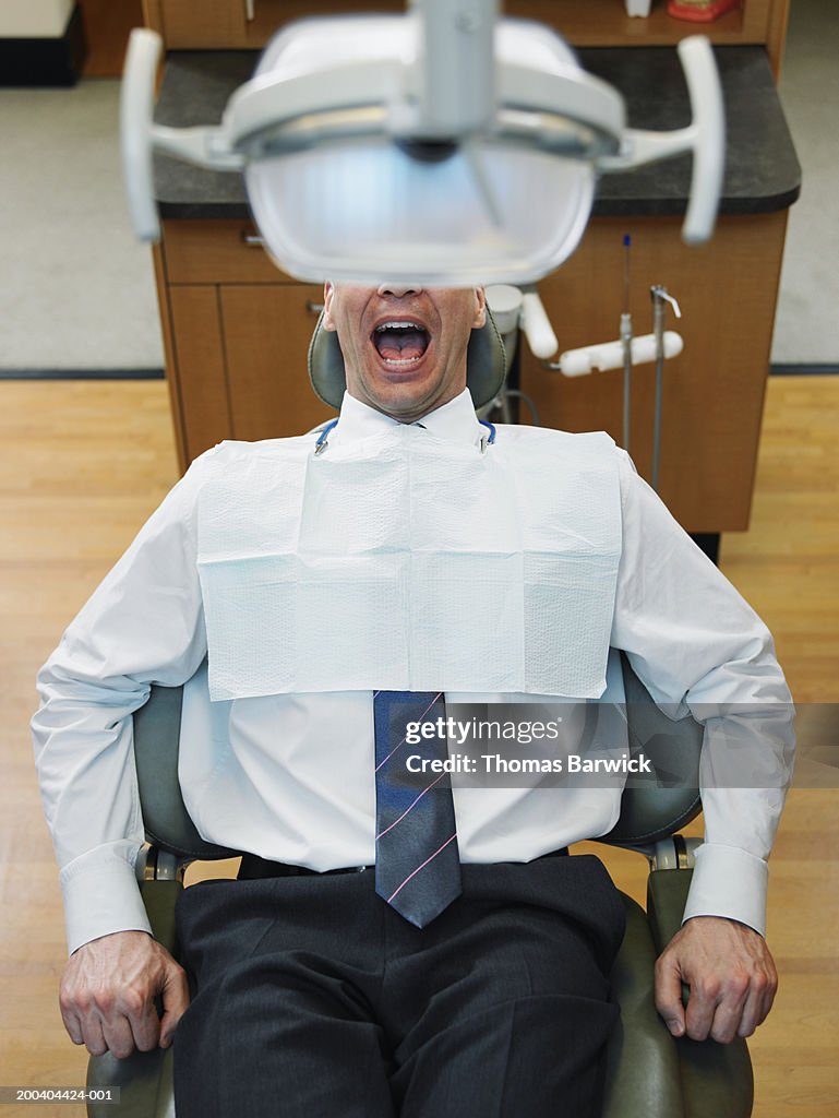 Mature man sitting in dentist's chair, mouth open, elevated view