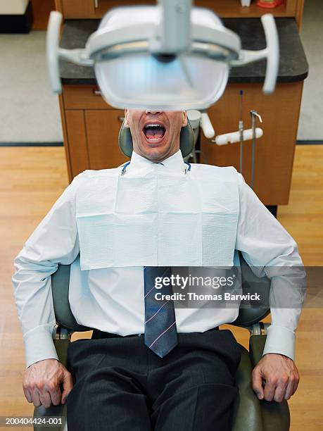 mature man sitting in dentist's chair, mouth open, elevated view - dentists chair stock pictures, royalty-free photos & images