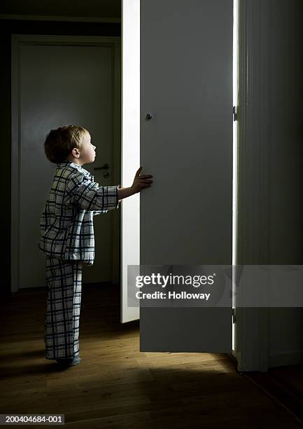 boy (2-4) opening cupboard doors standing in light - childrens closet stock-fotos und bilder