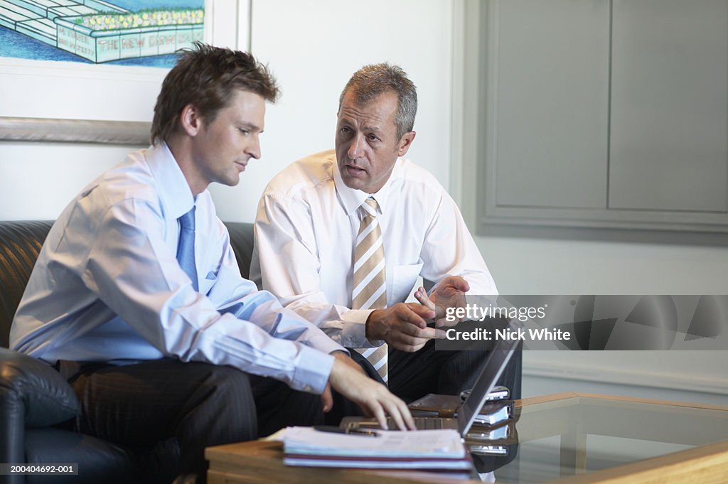Two businessmen having discussion on sofa in office waiting area