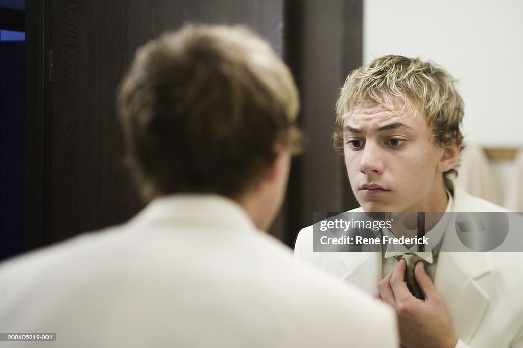 Teenage boy (14-16) adjusting tie in mirror