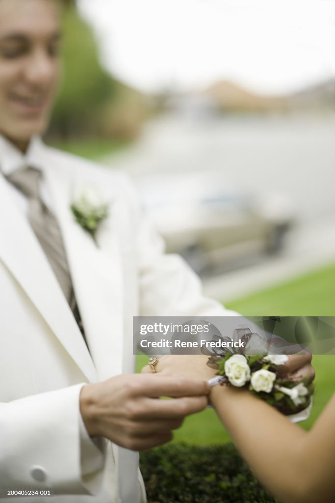 Teenage boy (14-16) placing wrist corsage on teenage girl (14-16)