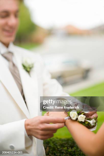 teenage boy (14-16) placing wrist corsage on teenage girl (14-16) - corsage imagens e fotografias de stock