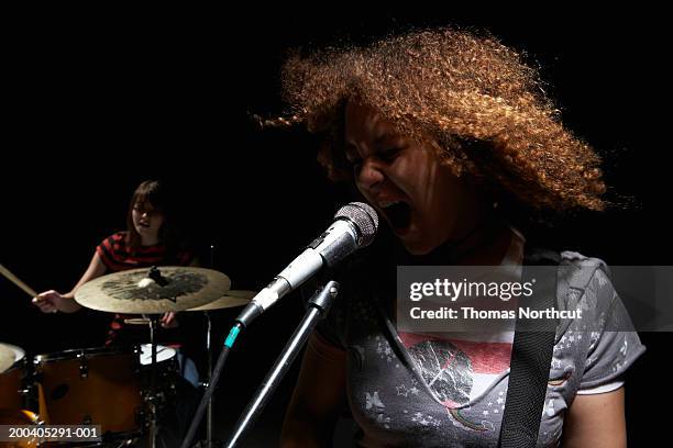 two teenage girls (14-16), one girl playing drums, one girl singing - girl singing imagens e fotografias de stock