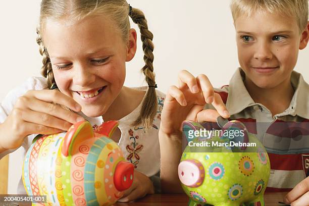 twin brother and sister (10-12) dropping coins into piggy banks, girl laughing, close-up - australian coin stock pictures, royalty-free photos & images