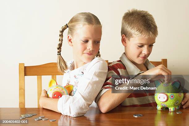 girl (10-12) watching twin brother drop coin into piggy bank - pocket money stock pictures, royalty-free photos & images