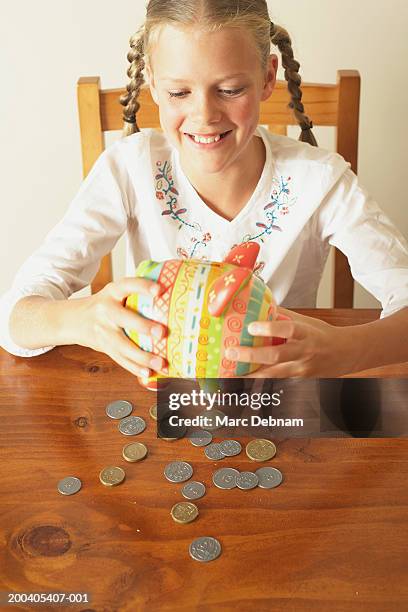 girl (10-12) emptying piggy bank onto table, smiling, elevated view - australian coin stock pictures, royalty-free photos & images