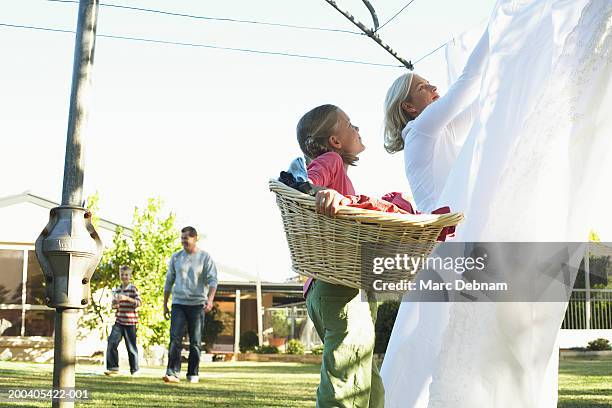 girl (10-12) with laundry basket looking up at mother hanging out washing - laundry basket fotografías e imágenes de stock