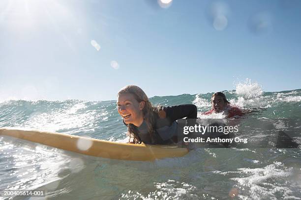 young man being towed in sea by young woman on surfboard, smiling - waves crashing foto e immagini stock