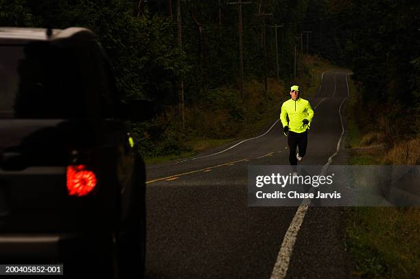 man jogging on road, car approaching, dusk - reflecterende kleren stockfoto's en -beelden